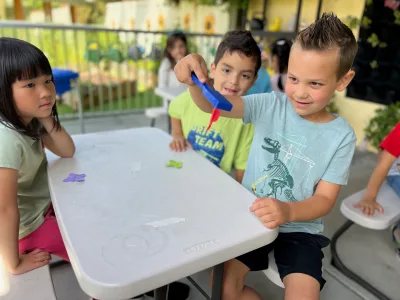 Child painting outdoors on canvas creating eco-art projects inspired by nature at Village Preschool Academy